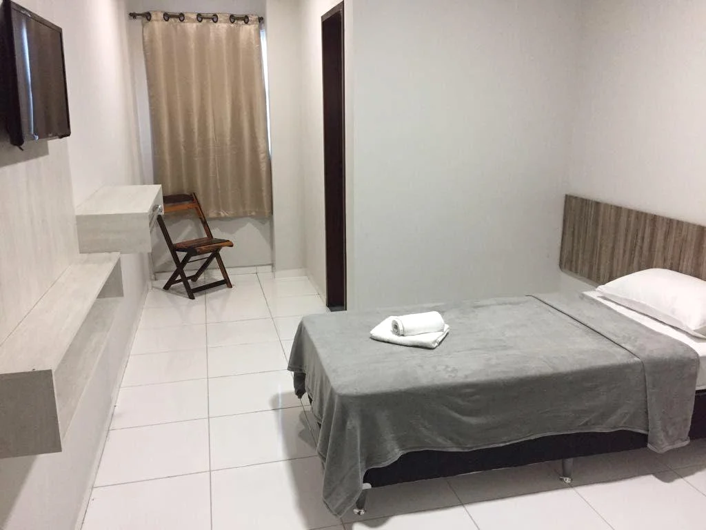 Acomodação com cama de solteiro, mesa de apoio, cadeira e TV
